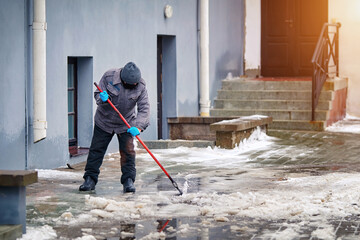 Man cleaning ice and snow with icebreaker tool. Janitor cleans area. Snow removal, winter road...