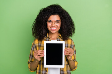 Photo of funky curly hairdo young lady show tablet wear eyewear checkered shirt isolated on green...