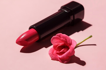 Obraz na płótnie Canvas Pink lipstick with a pelargonium flower on a pink background with a hard shadow.