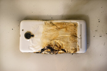 Fire consequences. Top view on a burnt mobile phone white on the table