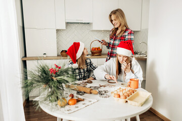 Mom and her daughters cook Christmas cookies or gingerbread together, family cooking of festive food. Merry Christmas and Happy Holidays