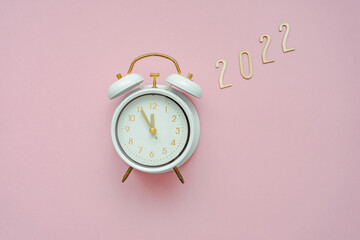 Ein Weicker mit fünf vor Zwölf  und die Jahreszahl 2022 auf einem pinken Hintergrund. Flat lay, Neujahr.