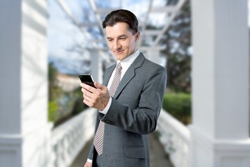 Young male freelancer walking near business center holding phone, smiling reading news,