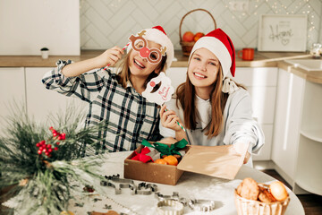 Two girls in Christmas hats are packing Christmas presents, sisters are having fun with Christmas masks