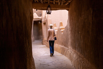 A lonely Western female tourist walking in the narrow street in Ushaiqer Heritage Village, Saudi Arabia. Back view.