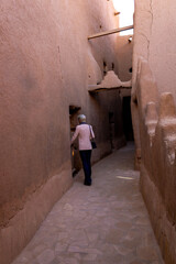 Obraz na płótnie Canvas A lonely Western female tourist standing in the narrow street in Ushaiqer Heritage Village, Saudi Arabia. Back view.