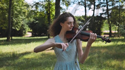 A young girl plays the violin in a city park. Video in motion.