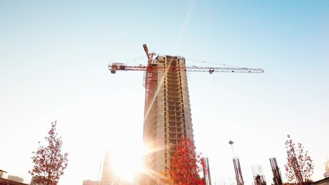 Tower crane at time laps construction site. Construction crane time laps. Construction of a multi-storey residential building with sunrise sunflare peak over building