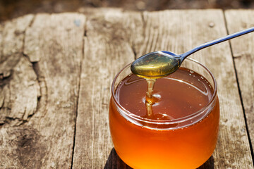 fresh summer honey in a glass jar with a spoon on the wooden table