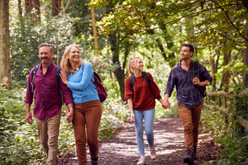 Mature And Mid Adult Couples In Countryside Hiking Along Path Through Forest Together