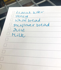 London, England - January 22 2021 - A shopping list on lined paper including peanut butter, honey, white bread, sunflower bread, juice and milk.  Image features intentional blur and has copy space.