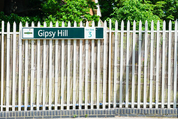 London, England - June 12 2021 - A sign for the Gipsy Hill rain station, affixed to a fence on a sunny summer day.  Gipsy Hill is a train station in South East London.  Image has copy space.