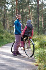 Young Sporty Mother and Little Daughter with Bicycle on the Wooden Path in a Forest
