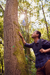 Man With Backpack In Countryside Hiking Along Path Through Forest Leaning Against Tree