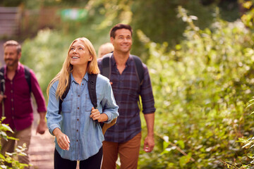 Mature And Mid Adult Couples In Countryside Hiking Along Path Through Forest Together