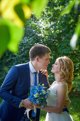 Young beautiful couple walk in nature in summer day. The bride in white dress with a long veil and a chiffon dress and a groom in blue suit. Wedding day in the park
