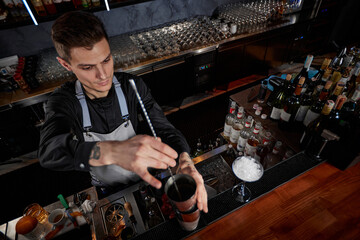 Barman stirring cocktail in shaker with spoon