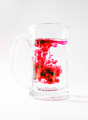 glass of water with red ink dropped in, swirls and twists, in a glass mug isoalted over white, studio photo shot, concept of chemistry or science experiments.