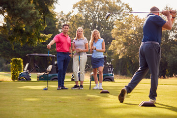 Mature And Mid Adult Couples Standing By Golf Buggy Watching Man Hit Tee Shot © Monkey Business