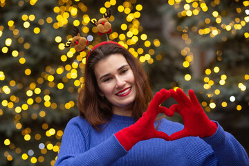 Happy lady at the Christmas tree showing heart sign