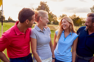 Obraz premium Mature And Mid Adult Couples Standing By Flag On Green Playing Round Of Golf Together