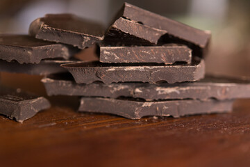 Broken pieces of dark chocolate on a wooden brown background.	