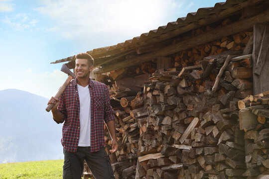 Happy man with ax near wood pile outdoors