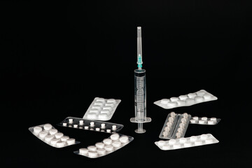 Medical pills in a plastic bag lie near the syringe. The syringe stands on a black background