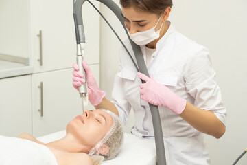 Naklejka premium Doctor cosmetologist makes a laser dermal rejuvenation procedure to a patient. Against the background of a medical office with copy space.