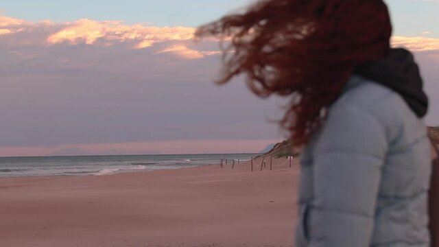 Woman with unfocused blue jacket observing a beach at sunset in winter