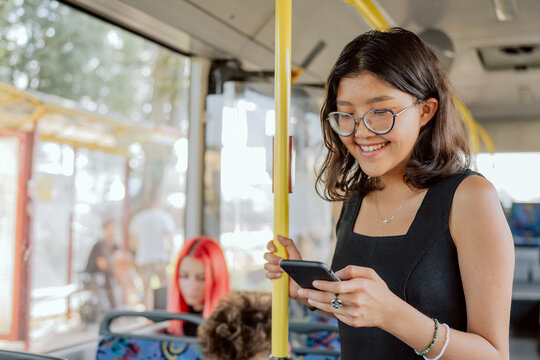 Bus stands at downtown bus stop woman with glasses taking public transportation clings to railing, looks at phone writes back to friends, browses social media occupie time during the long ride home