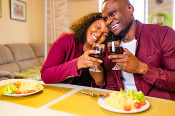 african american couple in love drinking wine from glasses and eating italian pasta in living room...