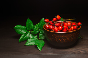 The studio shot of a red rose hips with green branch on dark wooden background. Healthy food concept