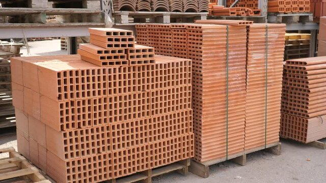 Pallets with stack of redbricks lying at warehouse of building materials in sunny day. High quality 4k footage