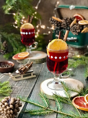 Two glasses of hot red mulled wine beverages with cardamom, cinnamon, clove, orange, anise, cranberry, fir needles. Seasonal winter beverage. Christmas decor. Selective focus, blurred