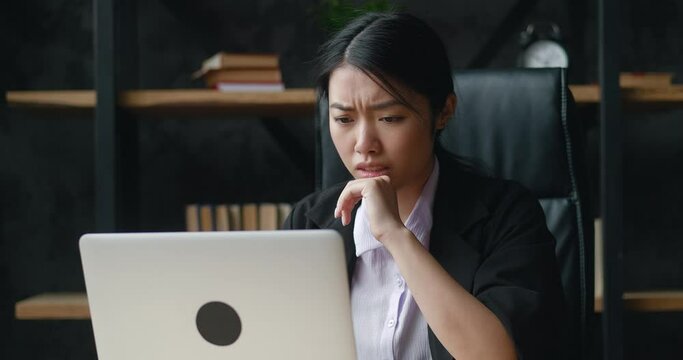 Shocked asian businesswoman upset with bad deal, looking at laptop screen, reaction on crisis. Unpleasantly surprised woman by the bad email seen on computer while working at office.