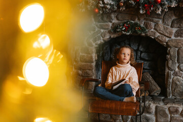 Obraz na płótnie Canvas Dreaming pensive little blonde curly child girl writing letter to Santa Claus sitting on chair by fireplace at home with festive interior. Pretty Caucasian kid writes letter with wishes for gift.