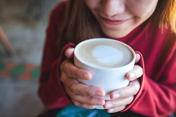 Closeup image of a young woman holding and drinking hot coffee