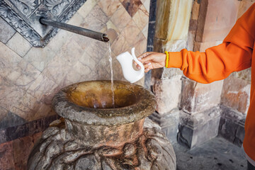 Woman pouring water in cup for drinking hot mineral therapeutic aqua. A resort for the treatment of...