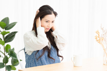 リビングで騒音に困って耳を塞いでいる主婦