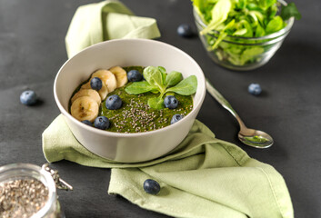 Green porridge in bawl with main ingredients: chia seeds, greens on the black background with napkin