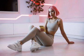 Beautiful woman with purple hair in futuristic costume with a smartphone in her hands. Smart home.