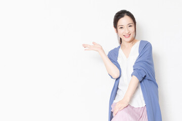 白い壁の前の椅子に座って案内のポーズをする主婦