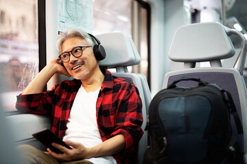 Senior man traveling by train. Man listening the music while enjoying in travel.