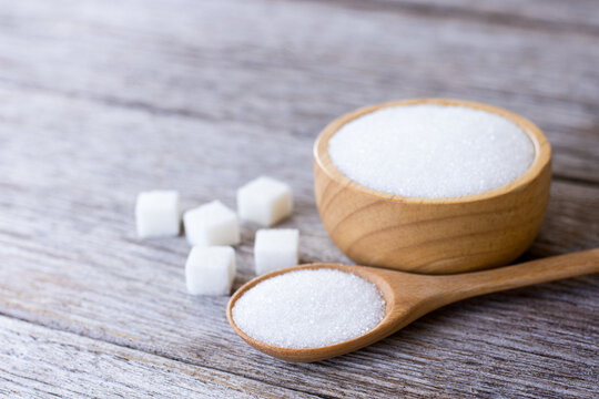 White sand sugar in wooden bowl and wooden spoon and cube sugar on wood table background.