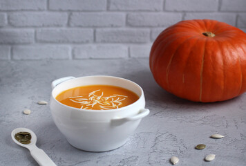 pumpkin soup with sauce and pumpkin seeds in a white cup on a gray background