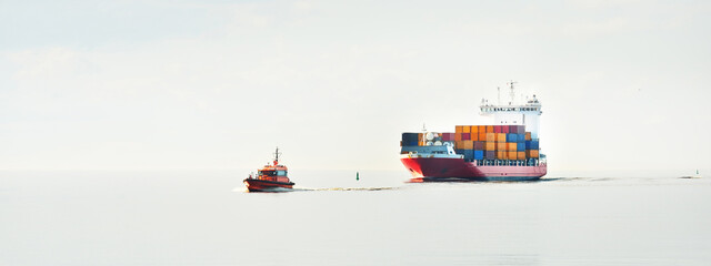 Large cargo container ship being led by the pilot boat. Piloting service. Unknown waters. Global...