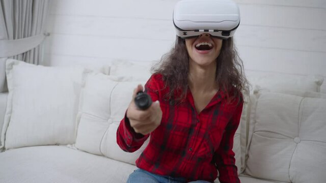 Excited Hispanic young woman wearing virtual reality headsets sitting on the couch playing a game with the consoles on weekend at home. slow motion POV footage.