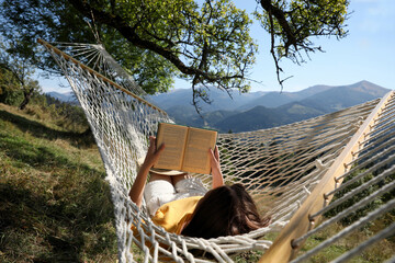 Young woman reading book in hammock outdoors on sunny day