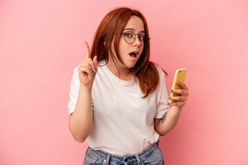 Young caucasian woman holding a mobile phone isolated on pink background having an idea, inspiration concept.